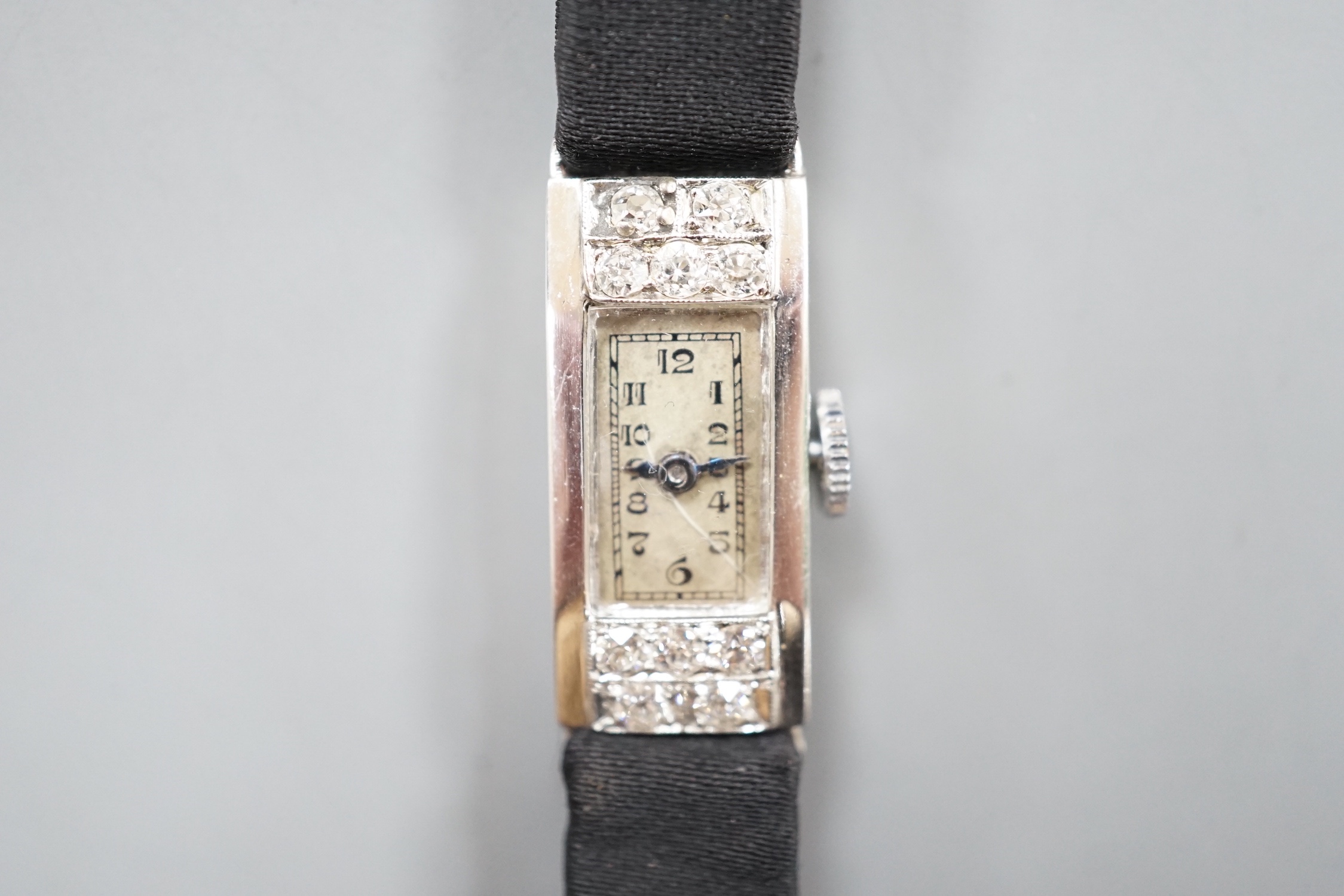 A lady's white meat (stamped Platinum) and diamond set rectangular manual wind cocktail watch, case diameter 11mm, on a black fabric strap, gross weight 10.3 grams.